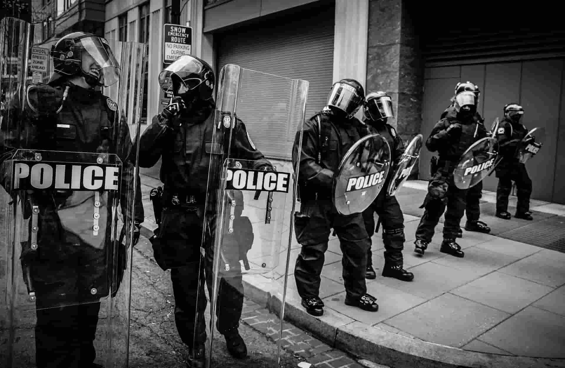 Policías en blanco y negro bloqueando una calle con escudos
