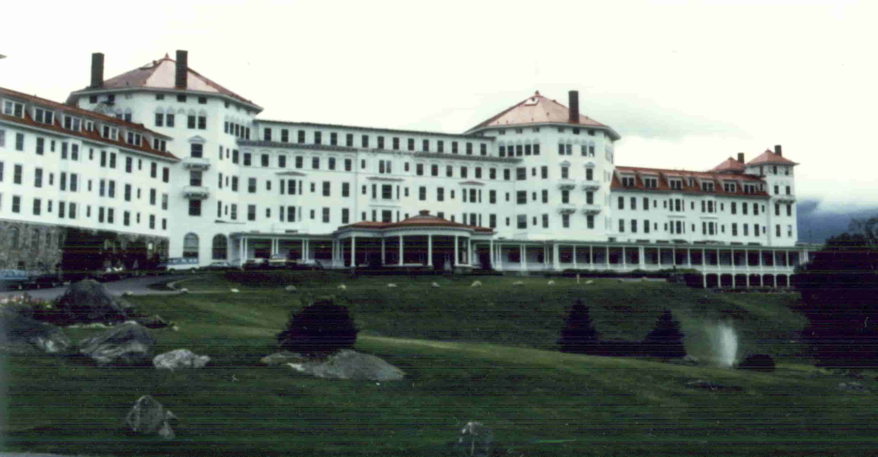 Un gran hotel de 5 plantas, con dos torres, y un gran campo de césped con colinas en la entrada