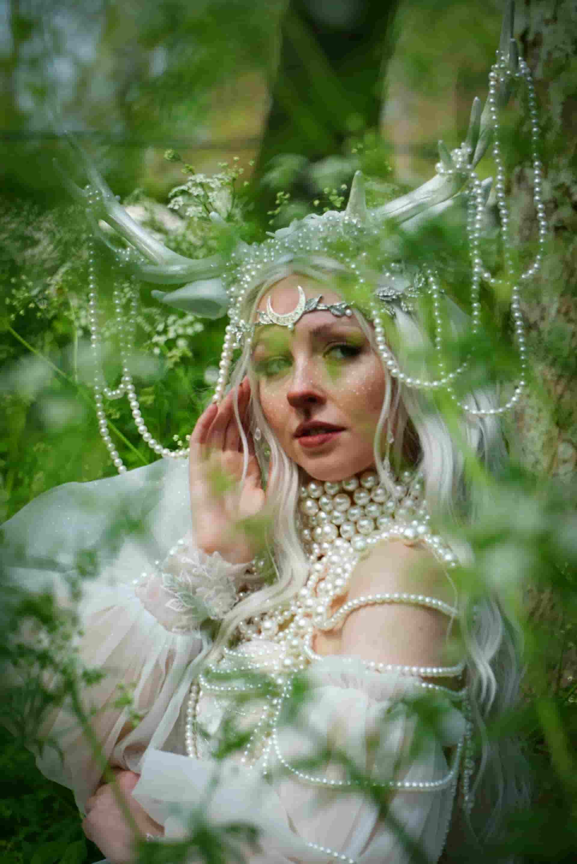 Una mujer vestida de blanco, con cuernos y collares de perlas por todas partes