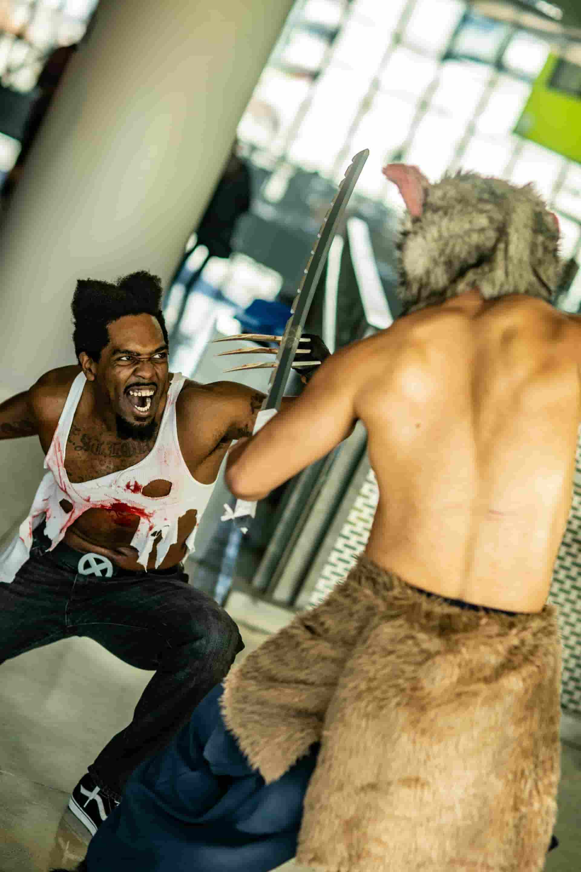 Un hombre con garras de lobezno luchando con otro con una cabeza de animal