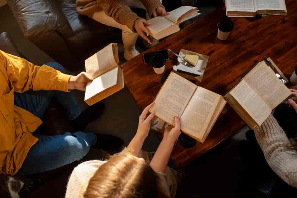 Varias personas sostienen sus libros abiertos por encima de una mesa de café