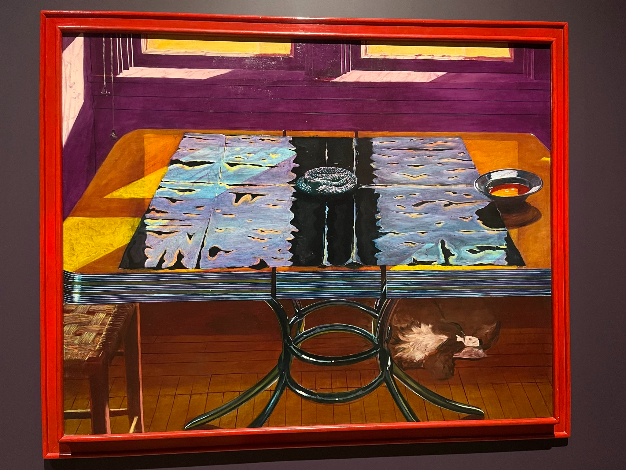 Picture of the painting Testament of the Holy Spirit by Eduardo Carrillo: an orange table with a snake and ashtray on top of it and a dog sleeping below. Light filters in from the window and the walls are purple