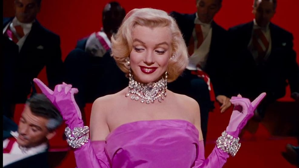 Still image from "Diamonds are a Girl's Best Friend" from "Gentlemen Prefer Blondes": Marilyn Monroe dressed in pink and many diamonds in front of suited dancing me