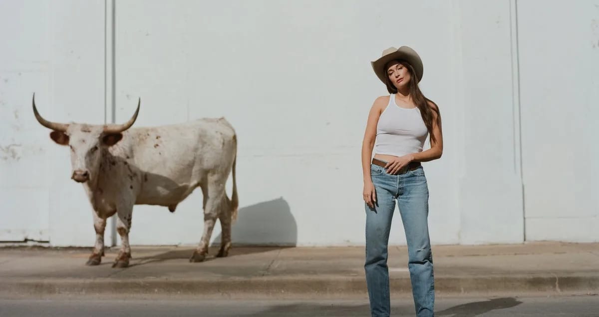 Kacey Musgraves stands next to a bull on a sidewalk.