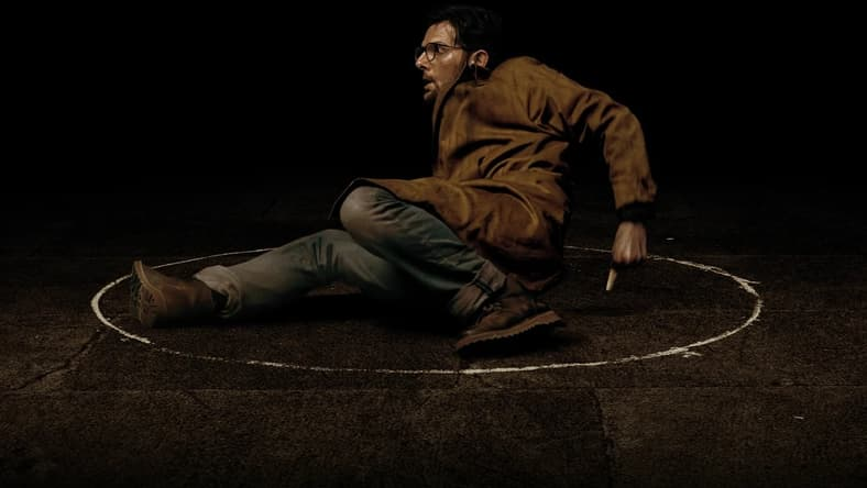Still from Hokum: Ohm (Adam Scott) sits on the ground with a white chalk circle around him
