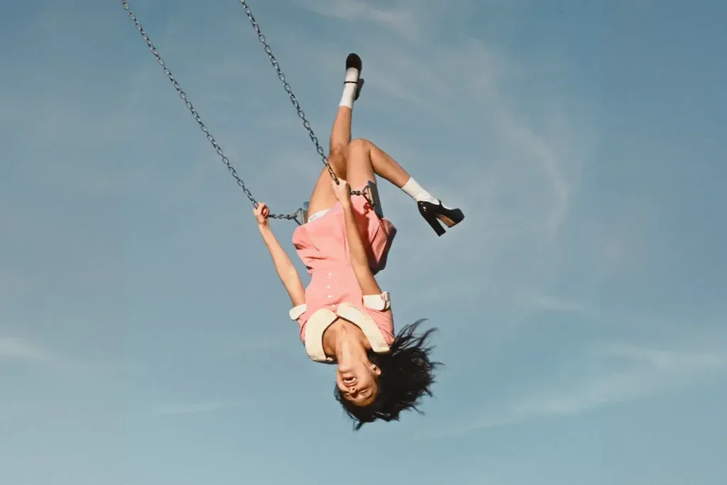 Cover of the album you seem pretty sad for a girl so in love by Olivia Rodrigo: Olivia is upside down on a swing against a blue sky
