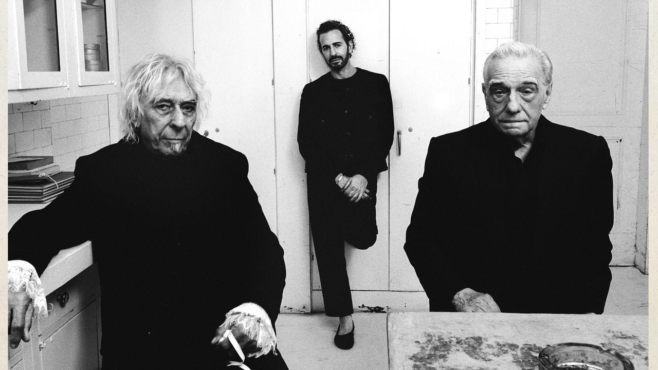Album art for Charli xcx's album "Music, Fashion, Film": a black and white image featuring John Cale, Marc Jacobs and Martin Scorcese in a small kitchen together