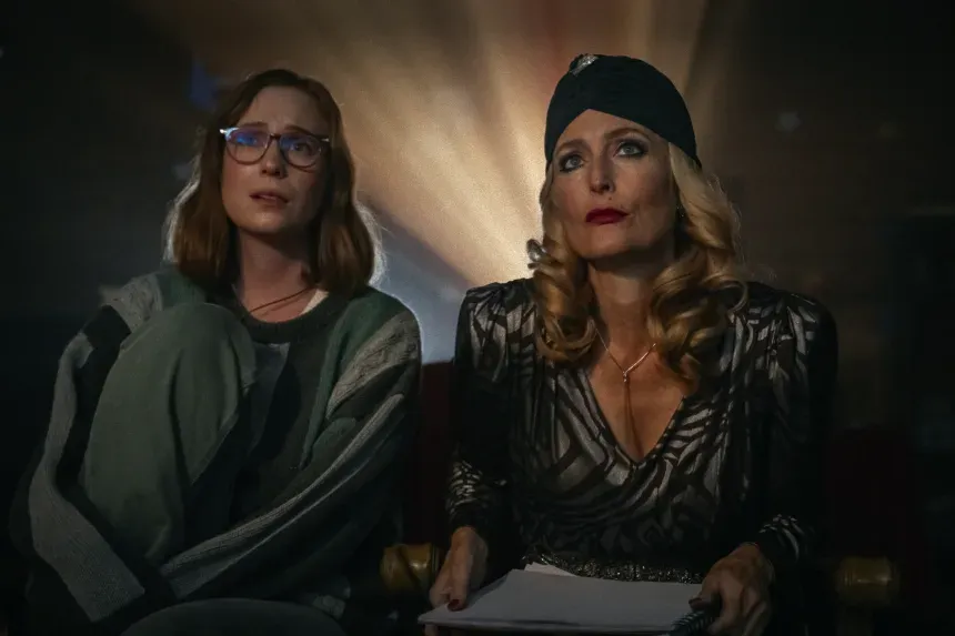 Still from the film Teenage Sex and Death at Camp Miasma: Kris (Hannah Einbinder) and Billy (Gillian Anderson) sit in a movie theather with a projector behind them.