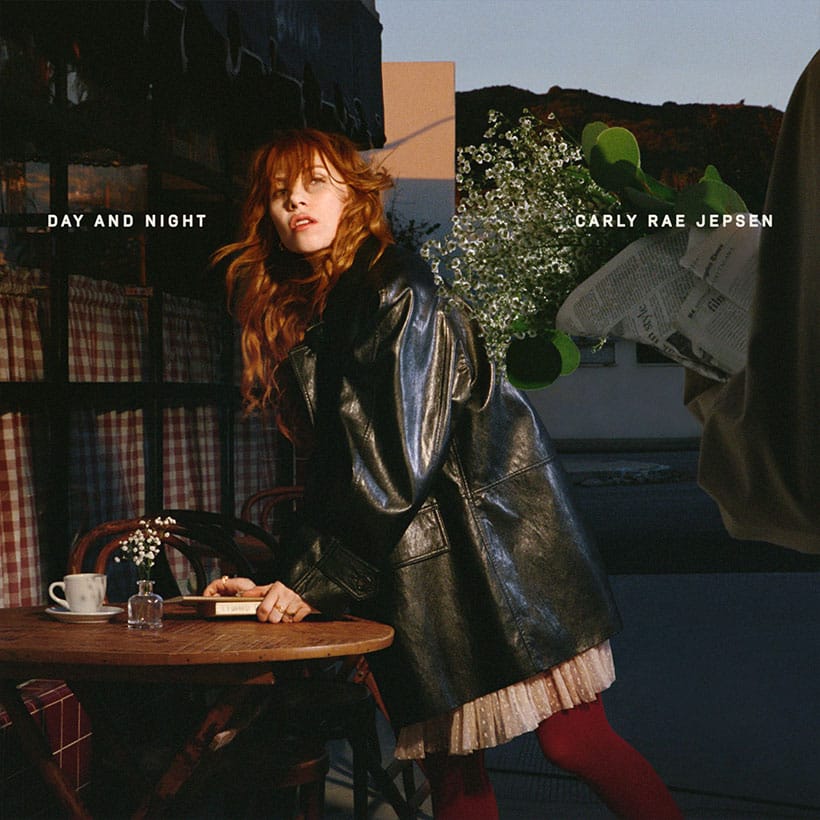 Cover for Carly Rae Jepsen's 2026 album "Day and Night" featuring Carly Rae Jepsen in a leather jacket leaning against a cafe table. It seems to be sunset.