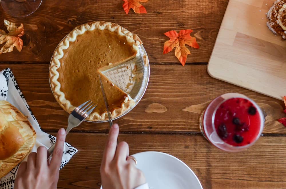 Cutting pumpkin pie at a wooden table with Fall decor.