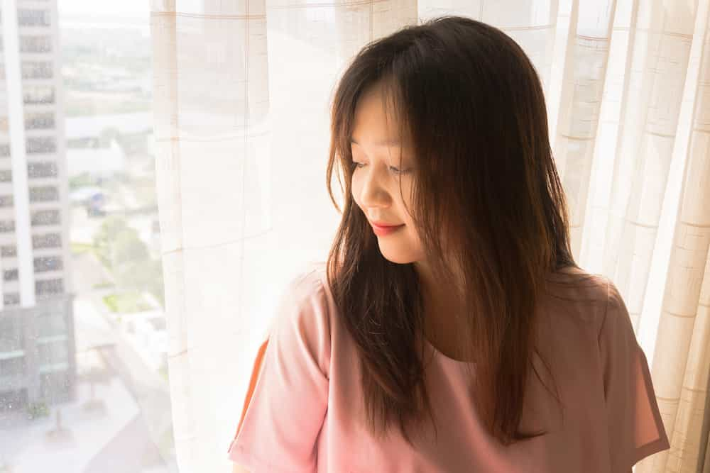 Woman looking out a sunny window and smiling.