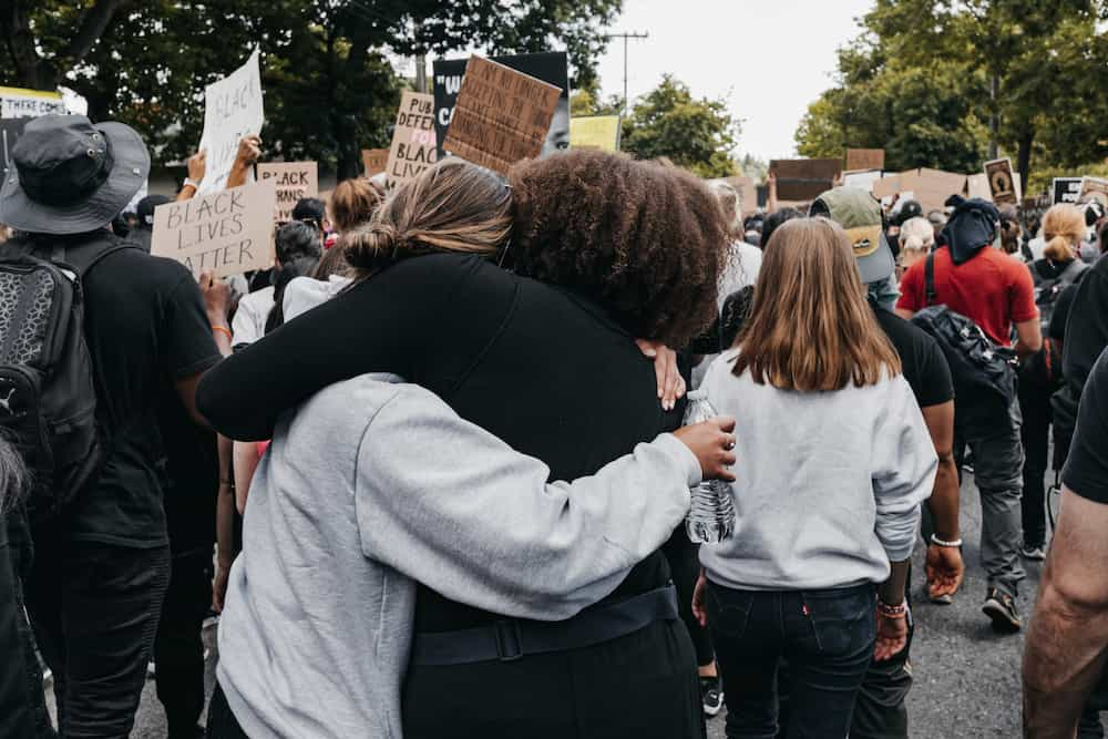 White woman and Black woman embracing during a rally.