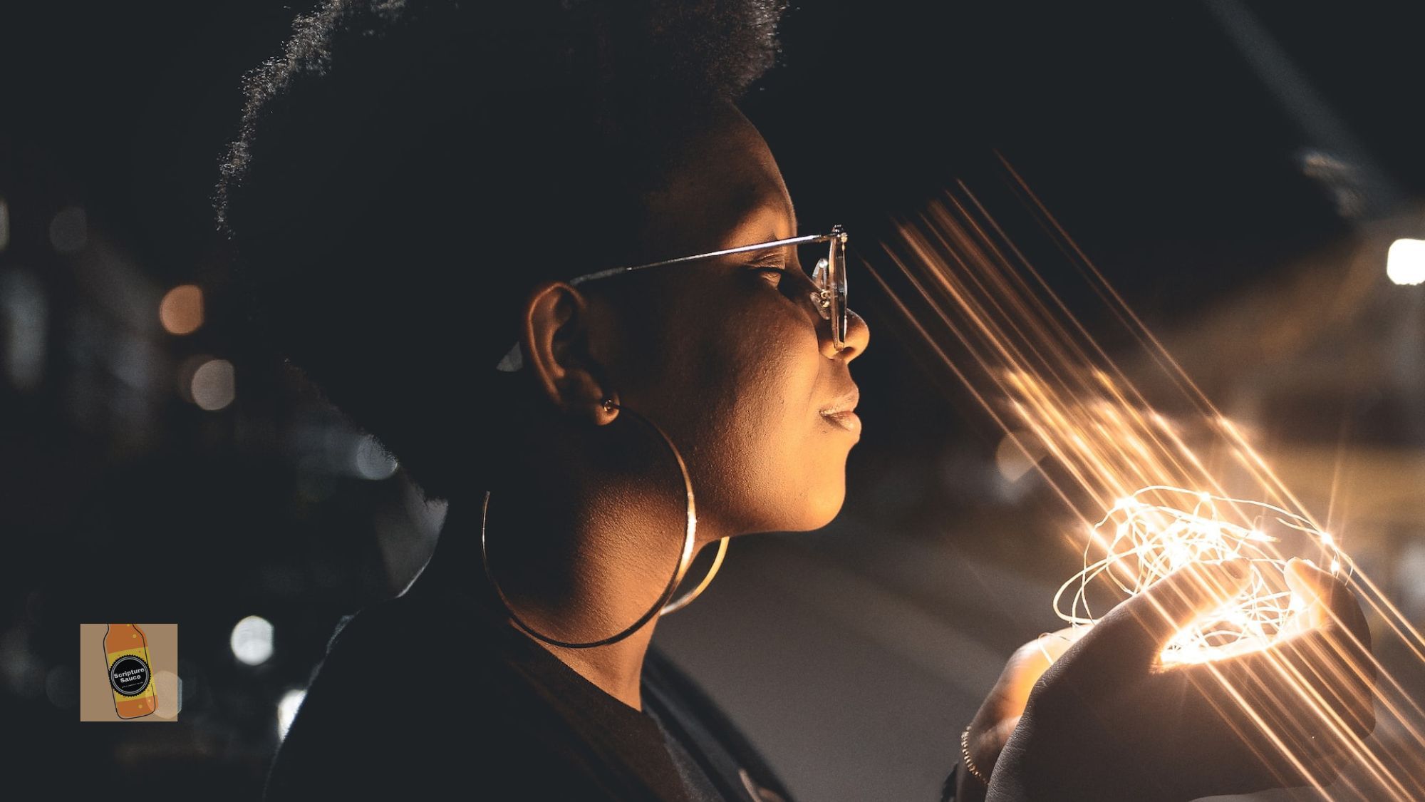 Black woman with contented smile as she holds warm, glowing strands of light.