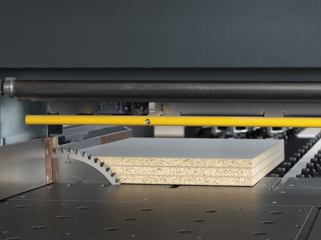 Detaliu cu pânza principală și pânza incizoare a unui fierăstrău de debitat, tăind un pachet (stack) de trei panouri de PAL melaminat.