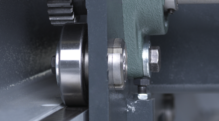 Detaliu macro al sistemului de antrenare al unui utilaj industrial, evidențiind un rulment de precizie, un angrenaj (pinion) și o structură metalică robustă.