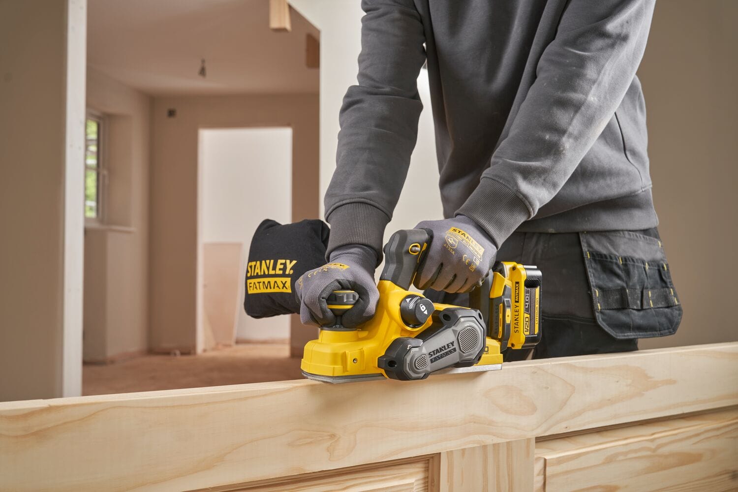 Tâmplar profesionist folosind o rindea electrică pe acumulator Stanley Fatmax V20 (model SFMCW300B) pentru a finisa o grindă sau un toc de ușă din lemn.