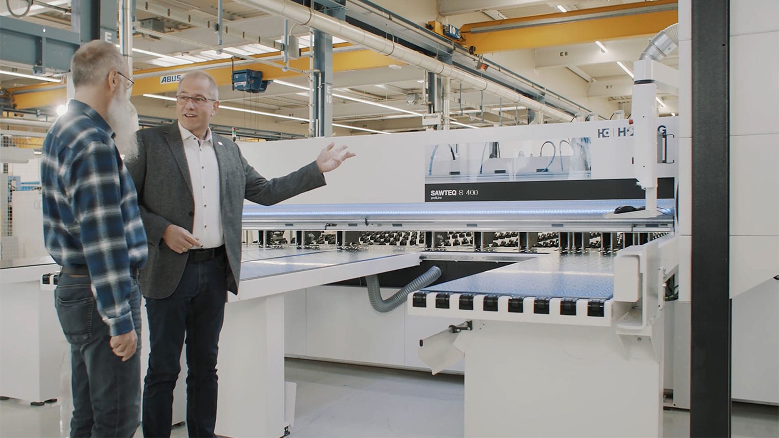 Un consultant tehnic sau inginer prezentând beneficiile fierăstrăului de debitat industrial HOMAG SAWTEQ S-400 unui manager de producție într-o fabrică modernă.