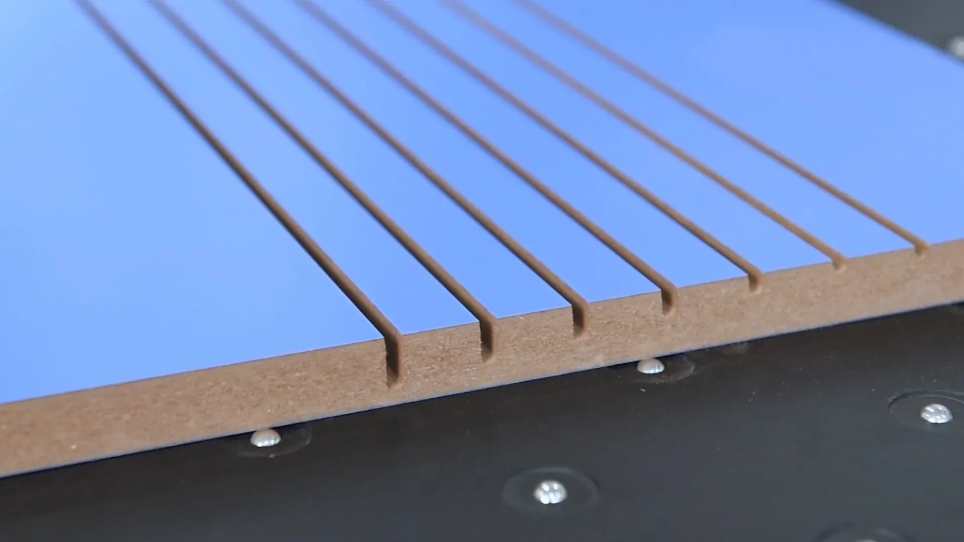 Detaliu cu un panou de MDF melaminat albastru, pe care au fost executate caneluri (nuturi) precise cu un fierăstrău de debitat sau CNC.